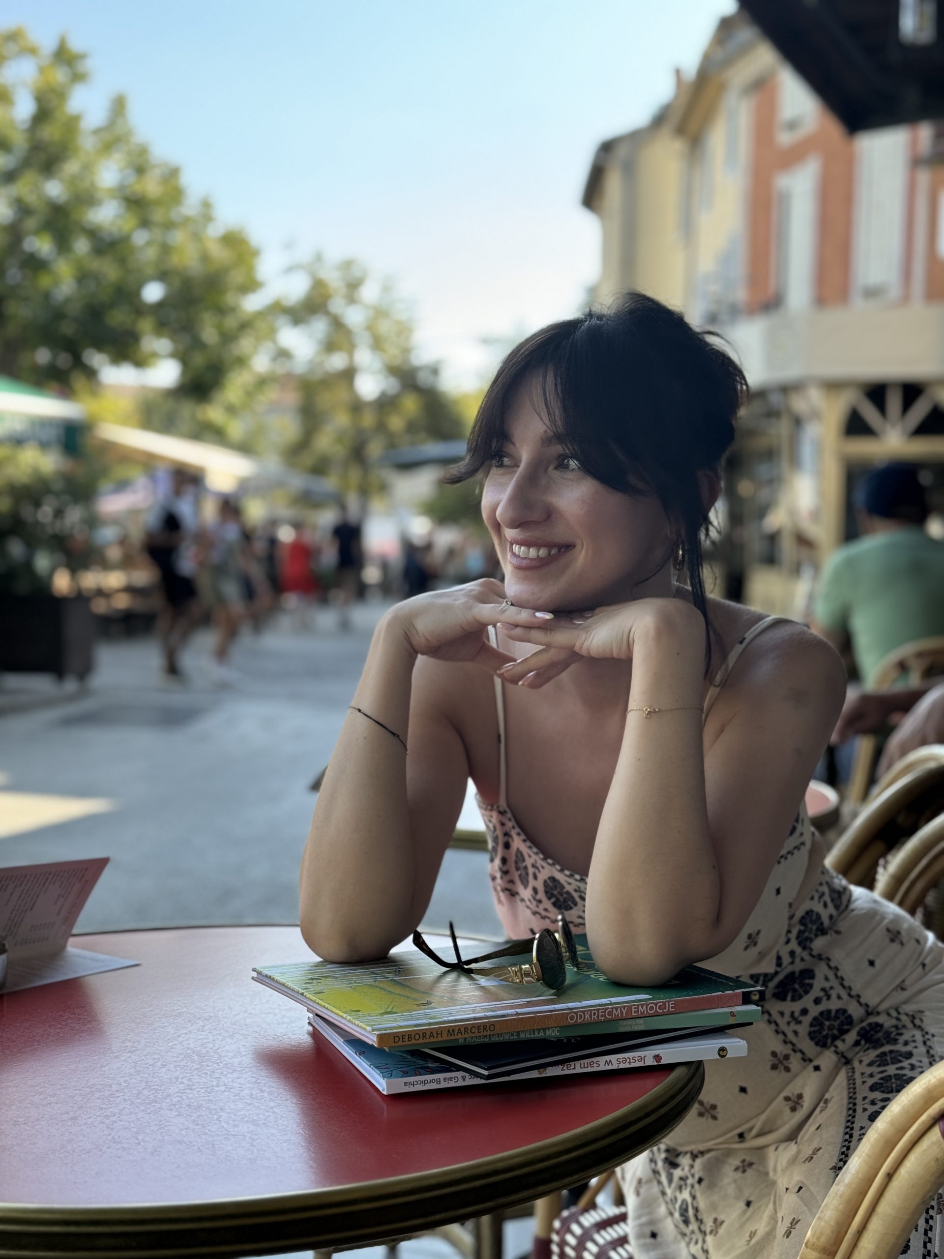 Natalia uśmiecha się przy kawiarni, mając ręce na książkach.